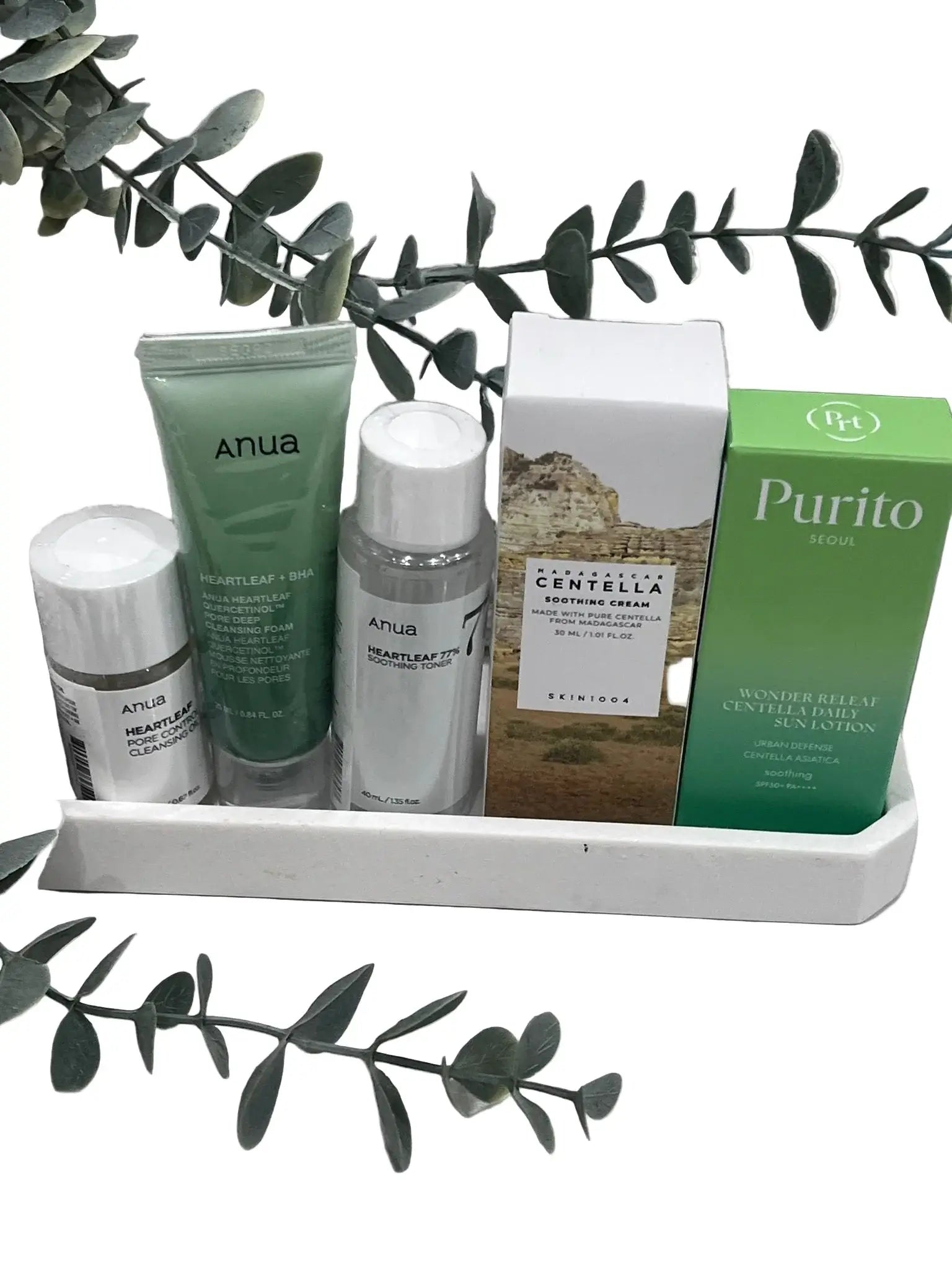 GlowTok Calm & Clear Teen Skincare Set with Purito and Anua products on white tray with green leaves.
